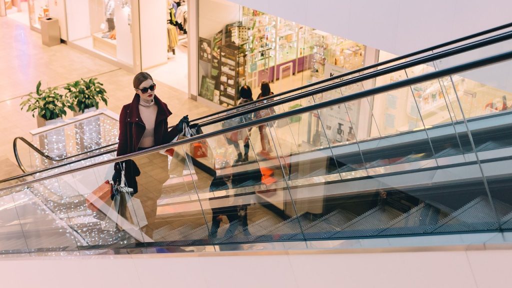 Kobieta z torbami zakupów na ruchomych schodach w galerii handlowej