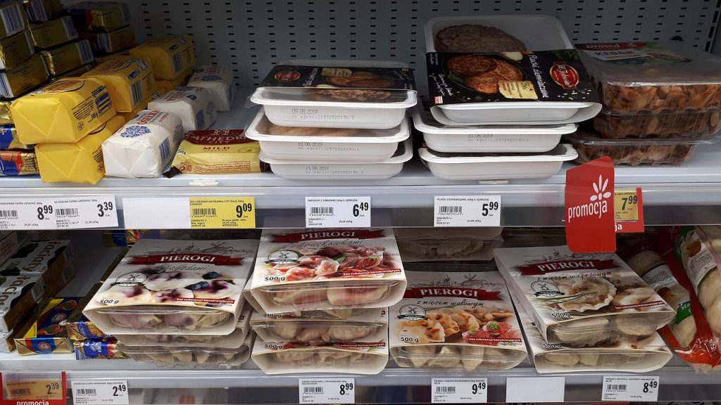 Półka chłodnicza w supermarkecie z masłem, pierogami i cenówkami promocyjnymi